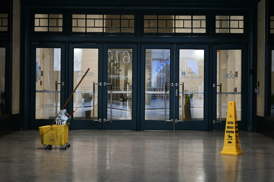 Yellow mop bucket and wet floor sign by glass doors.